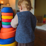 Ein Kleinkind stapelt von hinten gesehen eine Säule aus großen, bunten Schaumringen. Der Stapelstein: Mini Regenbogen Classic (6 Steine) zeigt lebendige Farben im Spielbereich, ideal für kreatives Spiel.