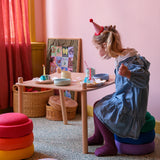 Kleines Mädchen sitzt auf einem Stapel Stapelstein: Regenbogen Classic (6 Steine) bei einer gemütlichen Teeparty, mit Kuchen und Kerzen vor sich, in einem kindlichen, stilvollen Spielzimmer von KLICKKLACK.