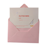 Geschenkgutschein analog: Eine hochwertige Karte in einem eleganten, geöffneten, hellrosa Kuvert. Der Gutschein, mit Feldern für Betrag und Ausstellungsdatum, repräsentiert stilvoll Freude und Nachhaltigkeit von klickklack.at.