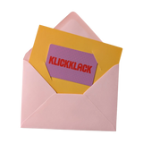 Geschenkgutschein analog: Eine geöffnete rosa Umschlaghülle enthüllt eine leuchtend gelbe Karte mit einem lila Einleger. Auf diesem steht KLICKKLACK in kräftigen roten Buchstaben, passend zum stilvollen, nachhaltigen Designanspruch des Geschäfts.
