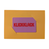 Geschenkgutschein analog: Ein eleganter Gutschein in Form einer lila Karte mit rotem KLICKKLACK-Schriftzug, stilvoll präsentiert in einem goldgelben Rahmen. Perfekt zum Verschenken von Freude und nachhaltigem Design.