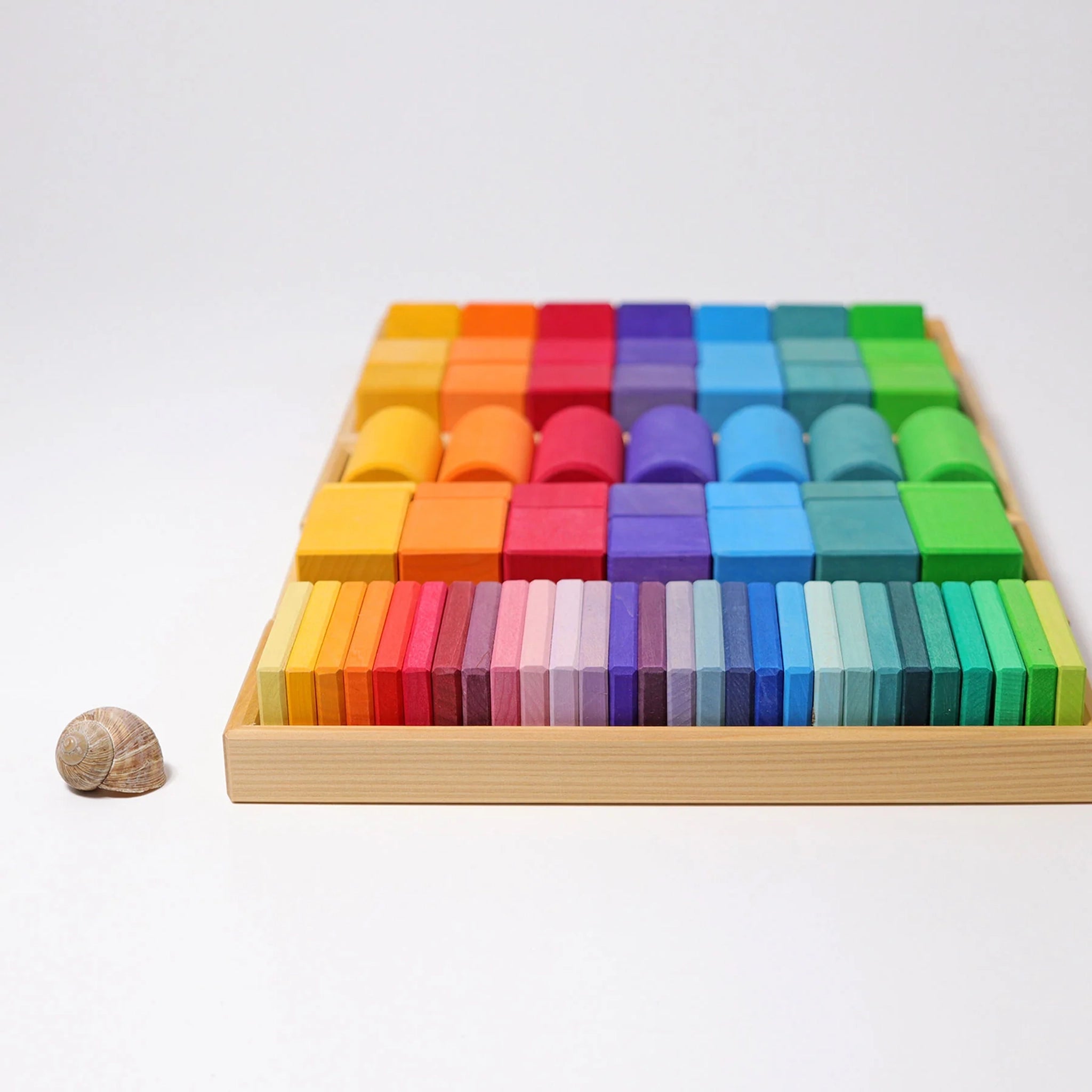 Bausteine: Formen und Farben – Ein flacher Holzrahmen enthält 70 farbenfrohe Bauklötze in verschiedenen Formen. Links daneben liegt eine Spiralschnecke. Ideal für kreatives Spiel und Farberkennung.