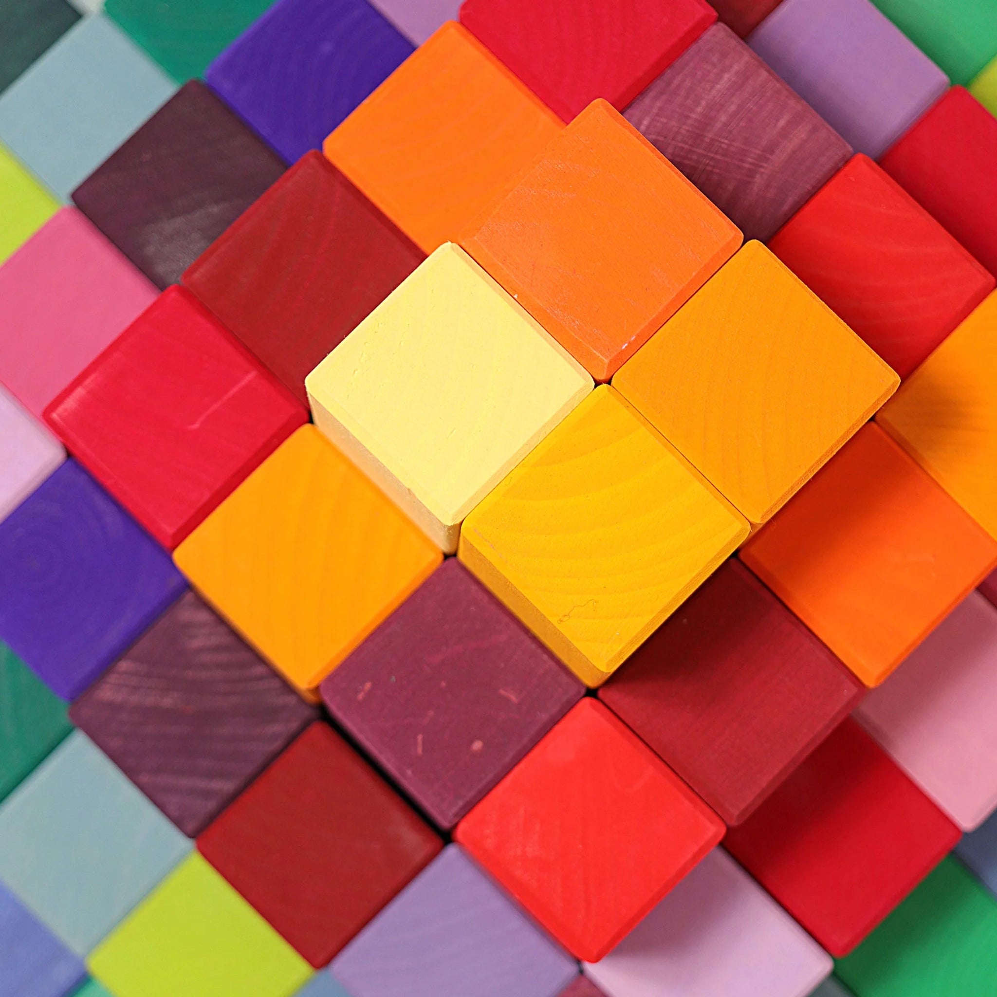 Freies Spiel: Große Stufenpyramide, ein künstlerisches Arrangement aus kleinen, bunt bemalten Holzblöcken, die in einem rasterförmigen Muster eine Herzform bilden. Ideal für kreative und nachhaltige Gestaltungsideen.