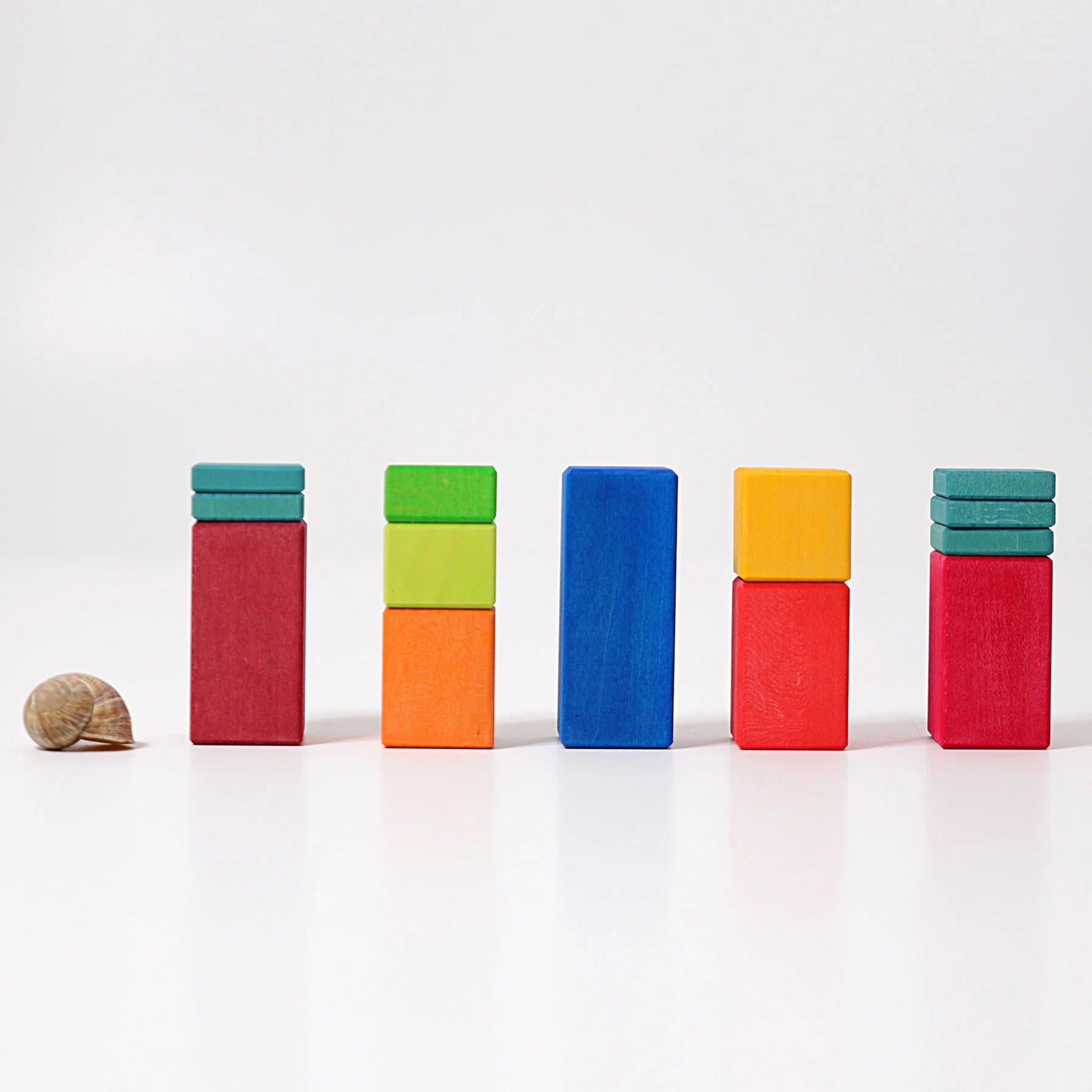 Freies Spiel: Große Stufenzählstäbe, fünf Türme aus bunten Holzklötzen in einer Reihe, links ein Schneckenhaus; fördert räumliches Denken und Mathematik, nachhaltig in Deutschland hergestellt.