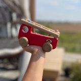 Holzfahrzeug: Feuerwehrauto aus robustem Buchen- und Ahornholz, gehalten von einer Kinderhand. Es zeigt eine hochklappbare Leiter und einfache Holzräder, hergestellt in einer kleinen polnischen Spielzeugmanufaktur.