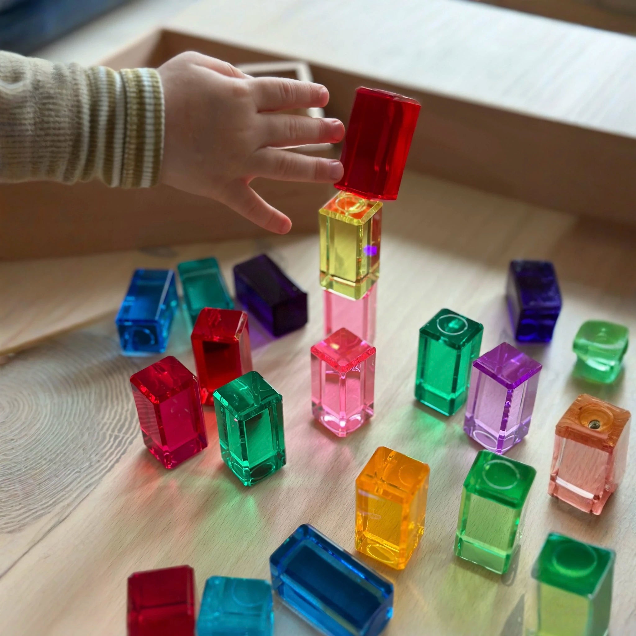 Kind spielt mit farbigen transparenten Bauquadern.