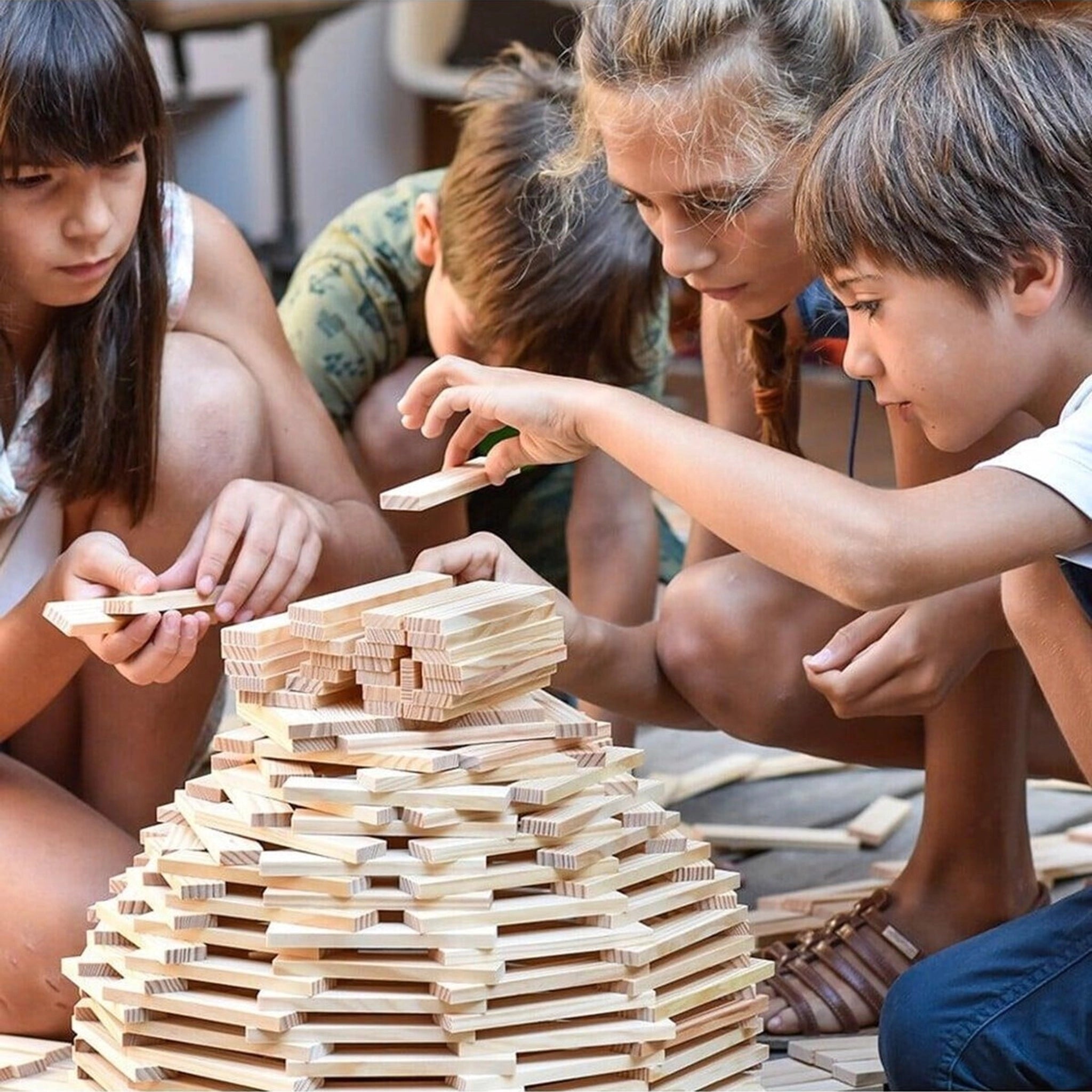 Kinder bauen konzentriert und kreativ eine hohe Struktur mit Bausteine: 500er Kiste, bestehend aus 500 nachhaltigen Pinienholzplättchen, die in einer stabilen Holzkiste von KLICKKLACK aufbewahrt werden.