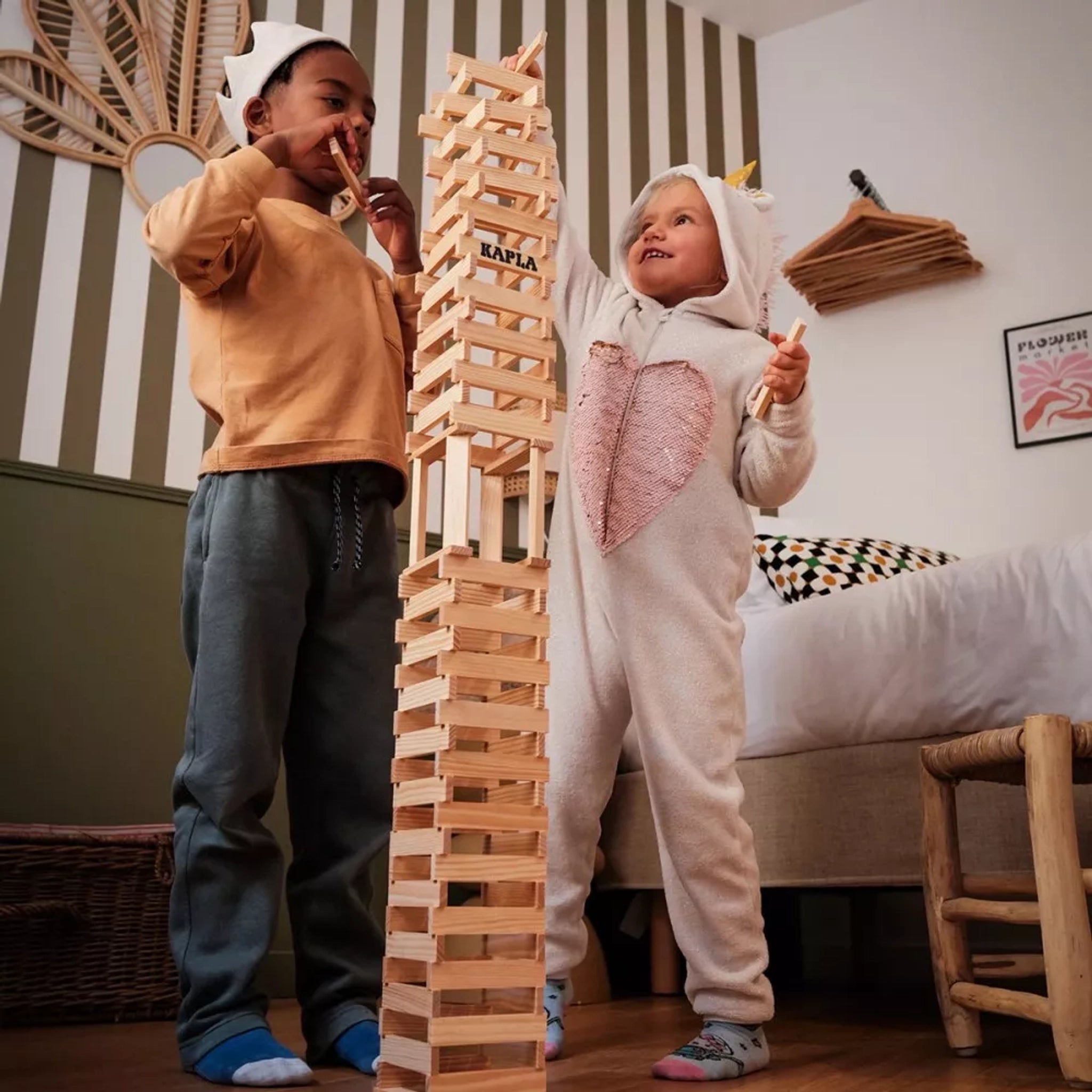 Zwei Kinder bauen einen hohen Turm aus Bausteine: 500er Kiste KAPLA-Plättchen in einem Spielzimmer. Diese nachhaltigen Pinienholzplättchen fördern Kreativität und räumliches Denken, geliefert in einer stabilen Holzkiste.