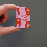 Hand, die ein Mini-Kaleidoskop im charakteristischen KLICKKLACK-Design hält, mit roten Buchstaben und Logo. Enthält hochwertige Materialien für kaleidoskopische Muster. Hergestellt in Spanien, vereint Ästhetik und Nachhaltigkeit.