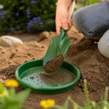 Nahaufnahme einer Person, die mit einem kleinen grünen Sandsieb von Redecker aus pulverbeschichtetem Metall Gartenerde in einem passenden grünen Behälter sichtet, ideal für Kinder im Sandkasten, Strand oder Garten.