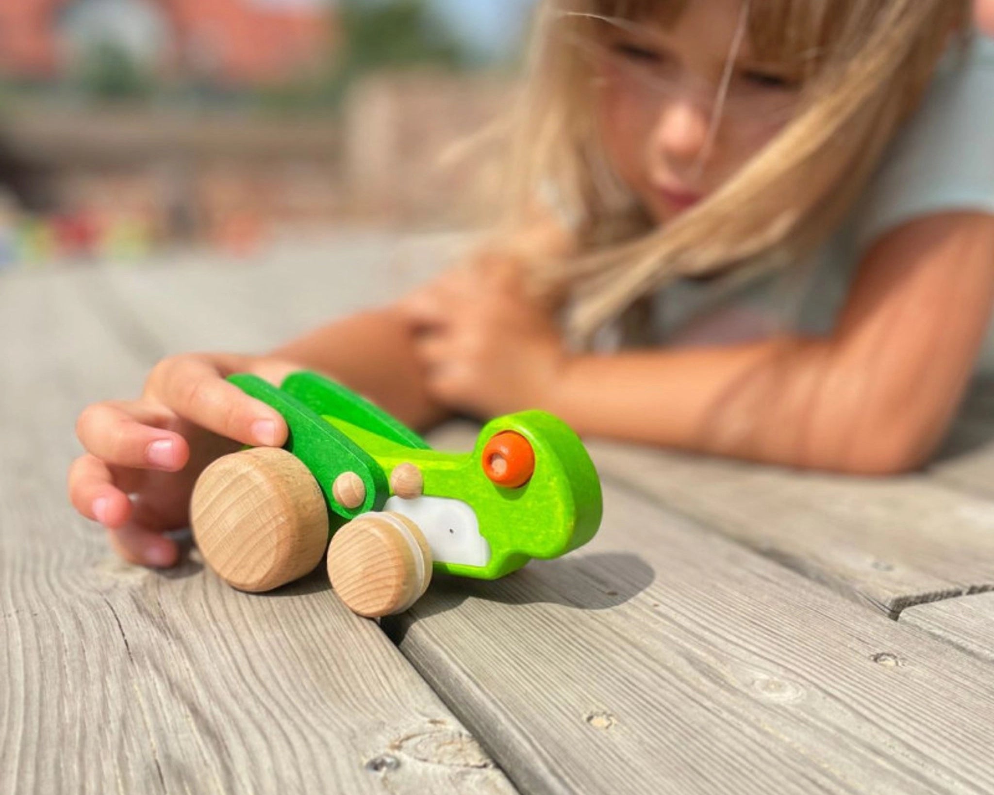 Kind spielt mit dem Rückziehspielzeug: Grashüpfer auf einer Holzterrasse. Das grüne Holzspielzeug hebt beim Zurückziehen seine Flügel. Hergestellt aus Buchenholz in einer polnischen Manufaktur.